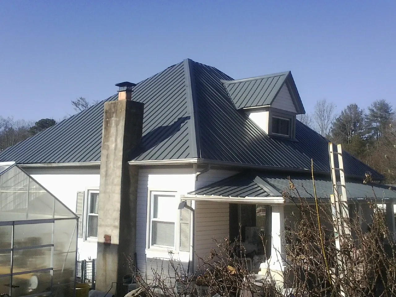 Dark blue standing seam metal roof on a white farmhouse with dormer — Slate & Tile Roof Repair by Roofing Brothers in Winnetka