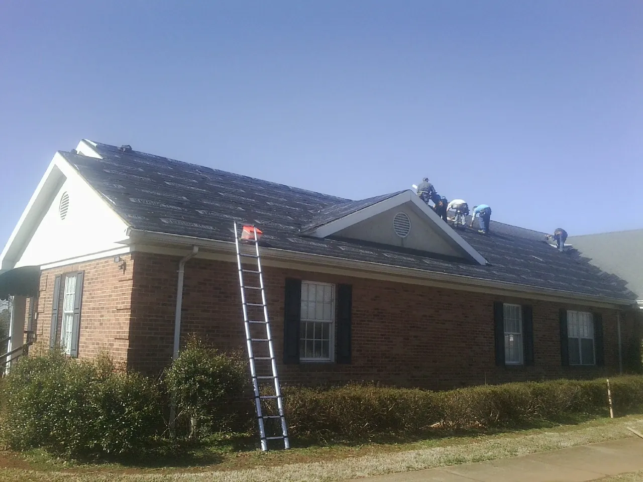 Crew tearing shingles off a brick ranch roof with a ladder set — Metal Roof Repair work by our crew in Winnetka