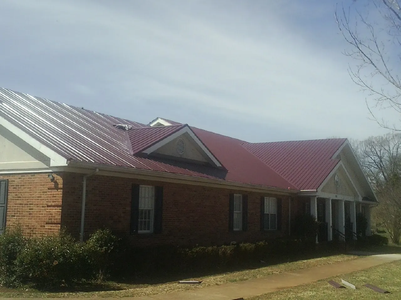 Red metal roof with gabled entries on a long brick building, from a Hail Damage Roof Repair job in Winnetka